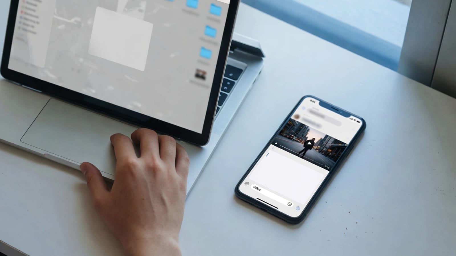 Hand on a laptop trackpad after a local compress, with a phone open to send the smaller video